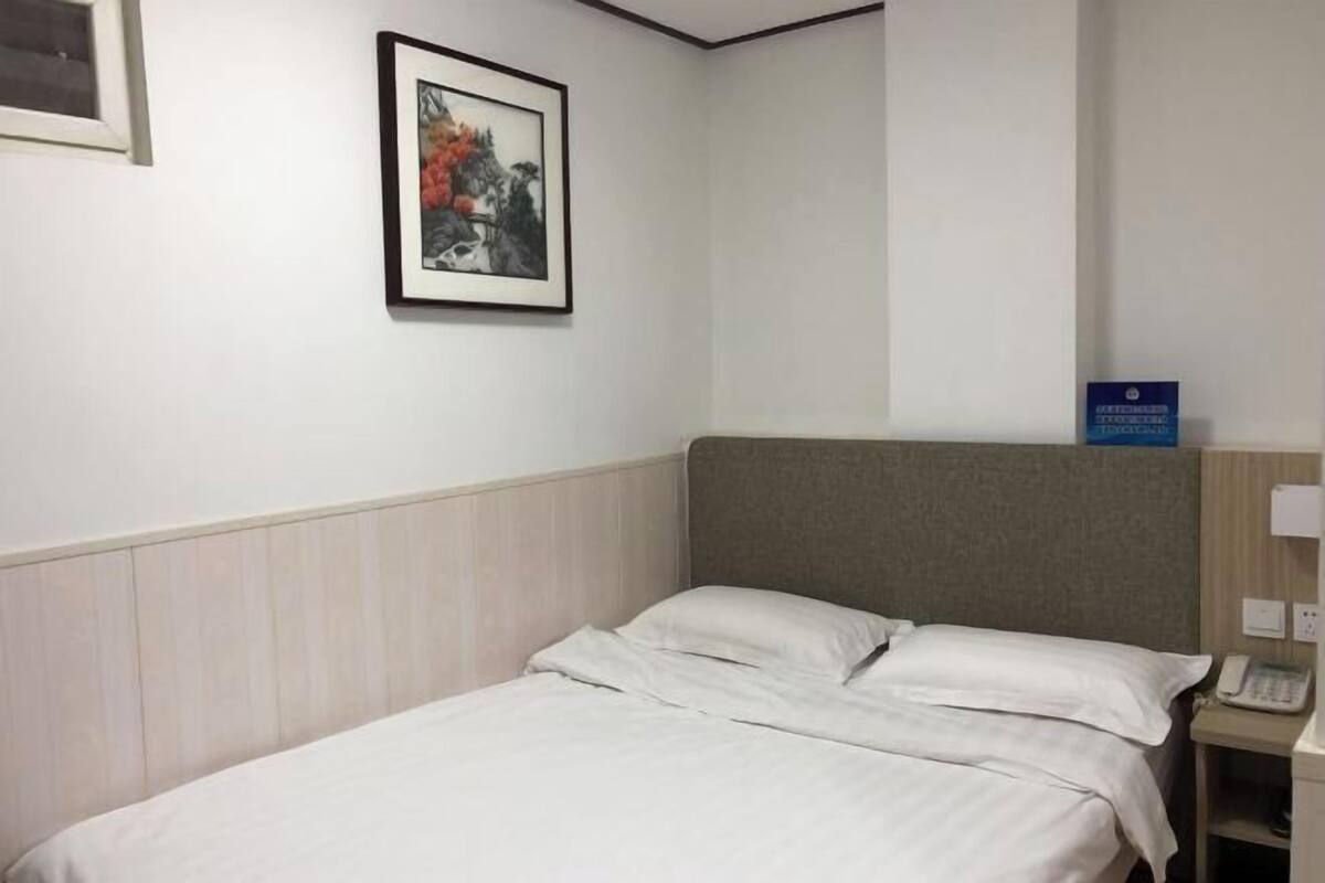A hotel room with a bed, a framed picture on the wall, a bedside telephone, and a sign indicating the room type.
