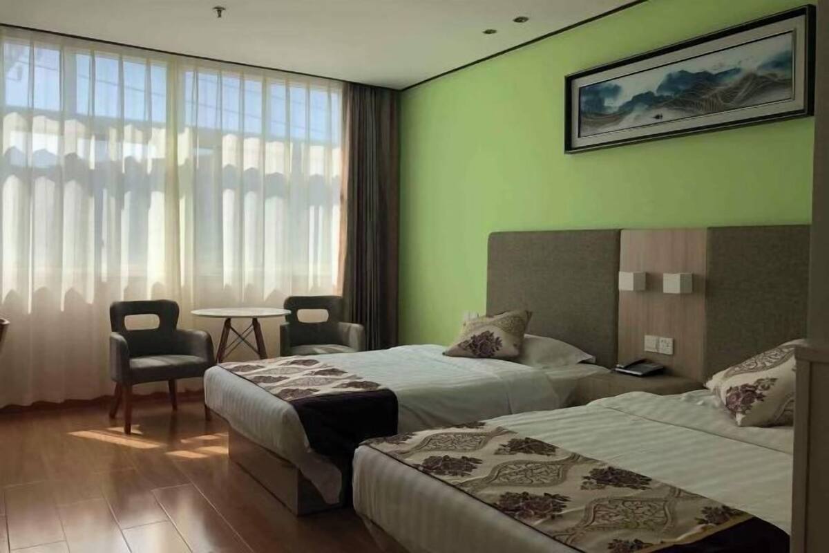 A hotel room with two beds, a small table, a chair, and a large window with curtains.