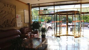 A lobby with a glass door entrance, a brown leather sofa, a glass coffee table, and a potted plant. - Nongjun Hotel (Beijing)
