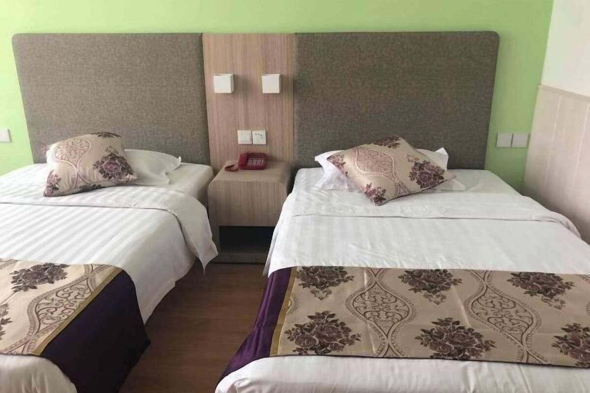 A hotel room with two beds, each with a floral-patterned bedspread, a wooden headboard, and a nightstand with a telephone.