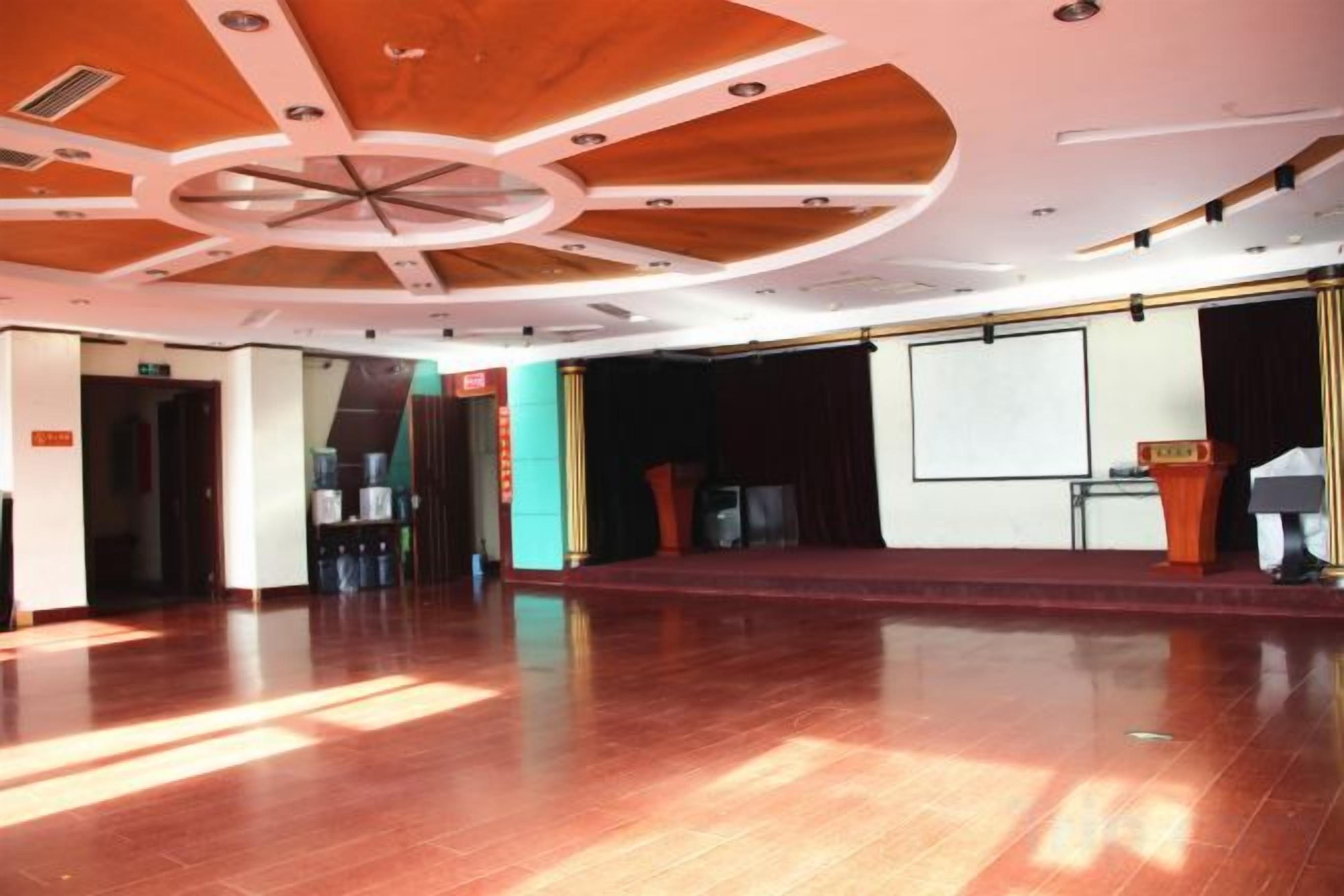A spacious hall with a polished wooden floor, a stage with a white screen, and a podium.