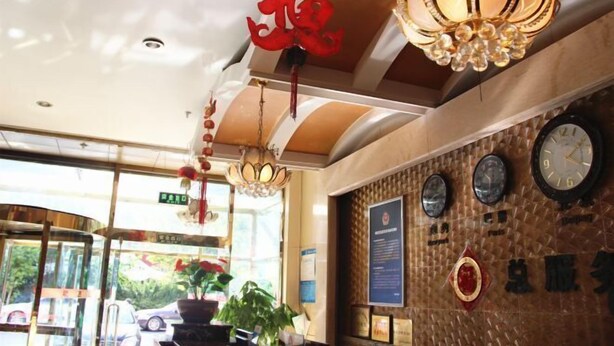A hotel lobby with a reception desk, a chandelier, clocks on the wall, and a large window with a view of the outside. - Nongjun Hotel (Beijing)