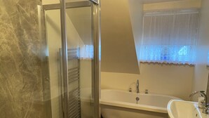 Un baño con una bañera independiente, cabina de ducha de vidrio y tocador con lavamanos.