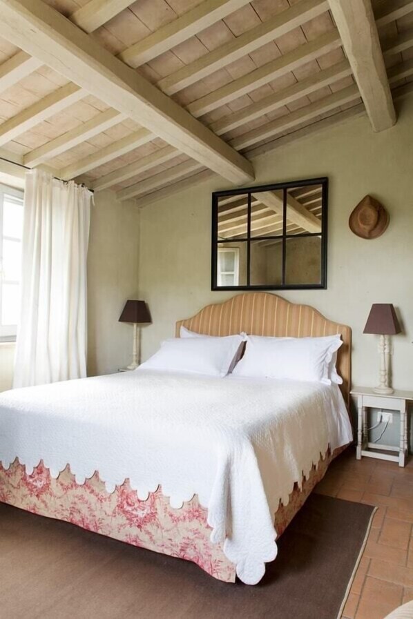 Une chambre à coucher avec un lit, deux tables de chevet, un miroir et une fenêtre avec des rideaux.