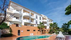 Ein mehrstöckiges Hotel mit Swimmingpool, Sitzgelegenheiten im Freien und Palmen.