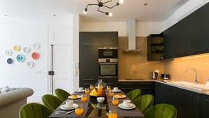 Una cocina moderna con armarios oscuros, una isla central y un comedor con sillas verdes.