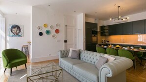 Una sala de estar moderna con un sofá azul claro, sillas verdes y una mesa de centro de vidrio.