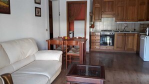 A living room with a sofa, a coffee table, and a dining table with chairs. There is a kitchen area with wooden cabinets and a stove. - Residential flat with garden (Scarlino)