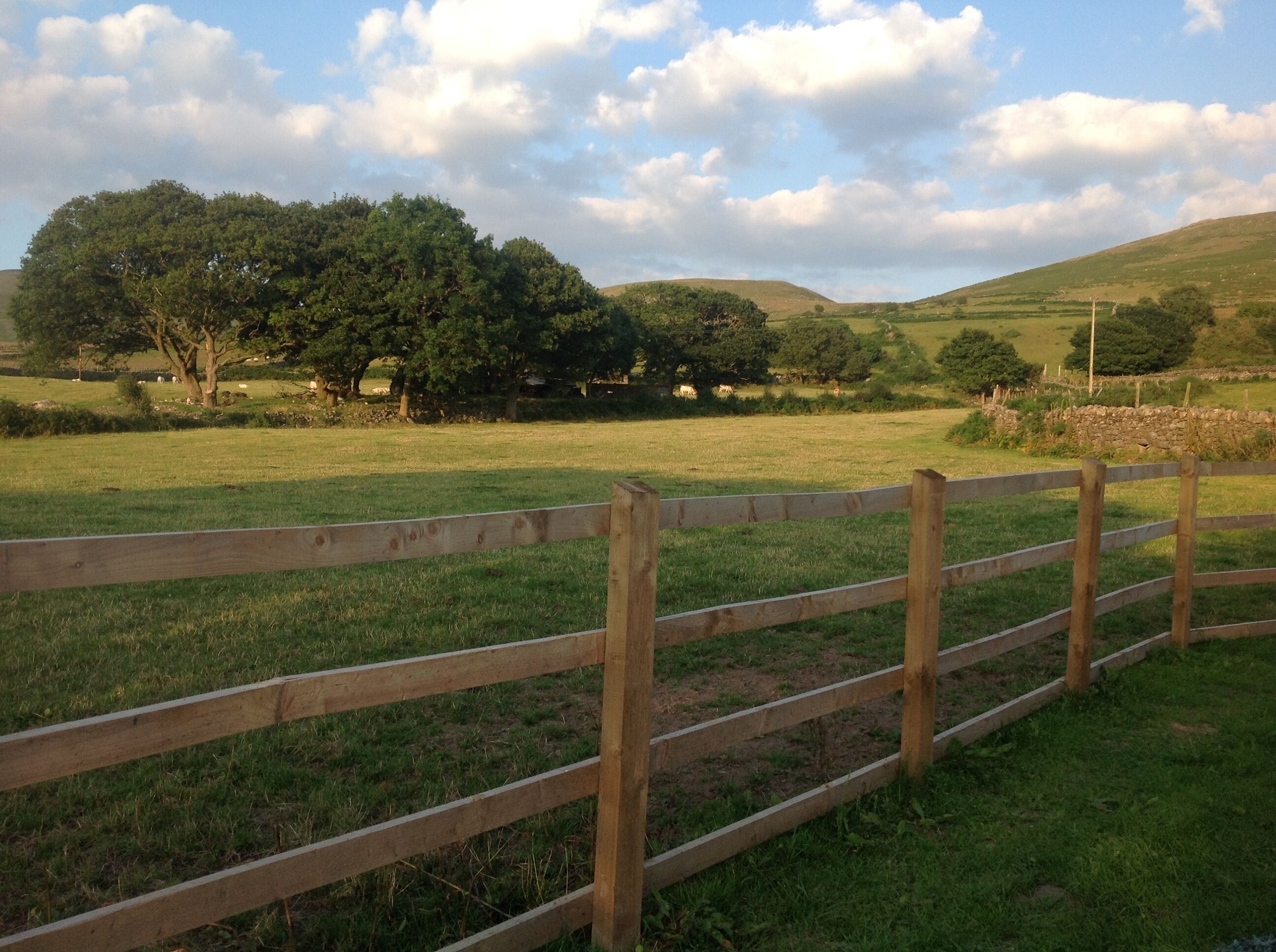 A wooden fence in a grassy field with trees and hills in the background.