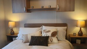A neatly made bed with a wooden headboard, flanked by two bedside tables with lamps, and a shelf above the bed.