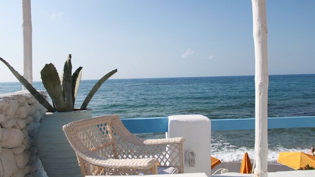 Una terrazza vista mare con una sedia in vimini, un vaso di fiori e la vista sull'oceano.