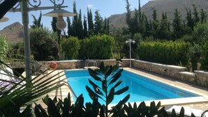Una piscina con borde de piedra, rodeada de vegetación y árboles, con montañas al fondo.