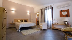 Un dormitorio con cama, mesitas de noche, una silla, escritorio, lámpara y aire acondicionado de pared.