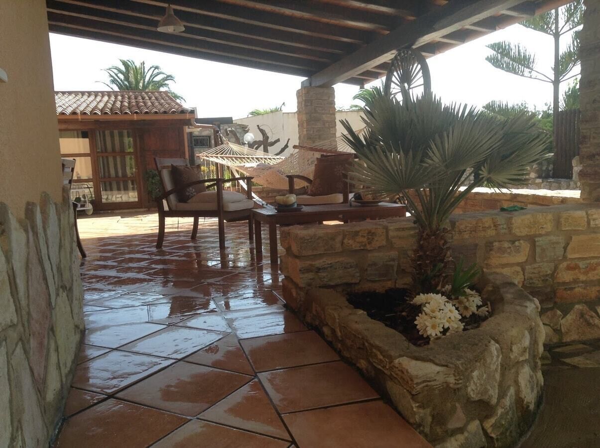 Un espace extérieur aménagé en patio, avec des murs en pierre, un hamac et un coin salon comprenant des chaises et une table.