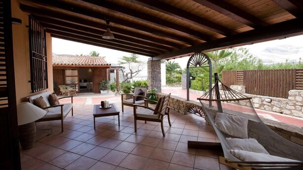 Un patio cubierto con mobiliario exterior, que incluye un sofá, sillas y una mesa.