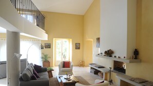 Ein geräumiges Wohnzimmer mit hoher Decke, Kamin und Balkon.
