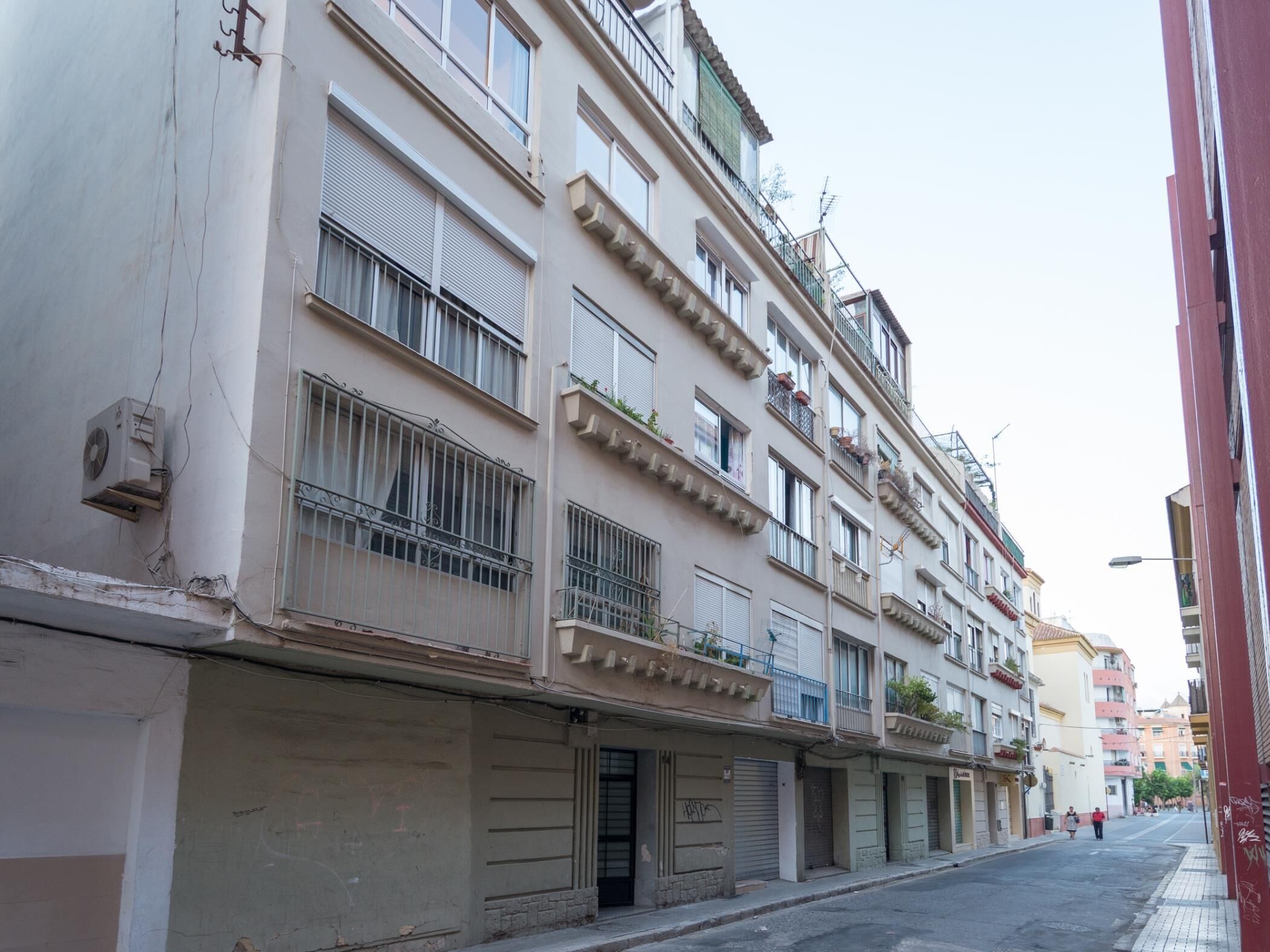 Ein mehrstöckiges Gebäude mit Balkonen, ein geschlossener Laden im Erdgeschoss und eine freie Straße davor.