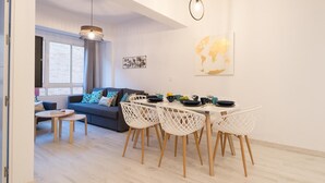 A modern living room with a sofa, a dining table with chairs, and a large window with blinds. - New Center 3Bedrooms 2 Bath Apartment (Malaga)