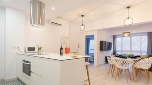 A modern kitchen with a central island, white cabinetry, and a microwave. There is a dining area with a table and chairs, and a TV mounted on the wall. - New Center 3Bedrooms 2 Bath Apartment (Malaga)