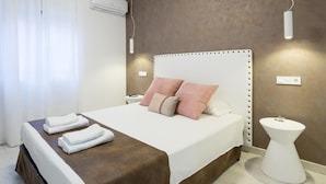 A modern hotel room with a large bed, white bedding, a brown headboard, and a bedside table with a lamp. - New Center 3Bedrooms 2 Bath Apartment (Malaga)