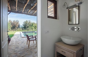 A bathroom with a large white sink, a mirror, and a window overlooking a pool area.