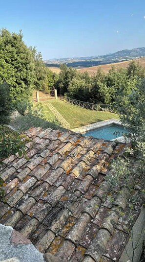 A rooftop with a swimming pool, surrounded by greenery and a clear view of distant hills.