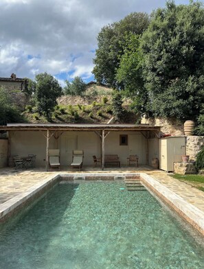 Une piscine aux eaux cristallines, bordée d’une terrasse en pierre, entourée de bancs en bois et dotée d’un espace de repos abrité.