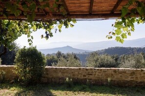 Un muro de piedra con vistas a montañas distantes y una pérgola de madera.