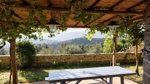 Un espace extérieur abrité, avec une table, un mur en pierre et une vue sur les collines.