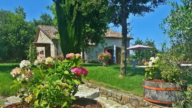 Un jardin avec un sentier en pierre menant à un bâtiment rustique surmonté d’un toit en tuiles.