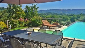 Un espace aménagé au bord de la piscine, avec une table et des chaises, un fauteuil de relaxation en bois et un grand parasol.