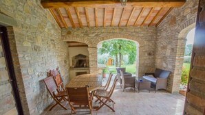 Une terrasse extérieure avec des murs en pierre, une table en bois avec des chaises et une vue sur un jardin.