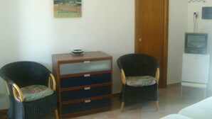 Una habitación pequeña con dos sillas, un armario de madera, un televisor y una puerta.