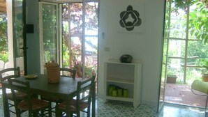 Un comedor con mesa y sillas, una estantería con un altavoz y una ventana con vistas a zonas verdes.