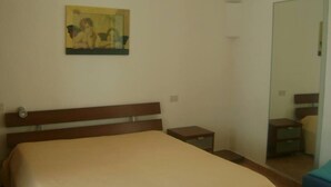 Un dormitorio con cama, mesita de noche, una pequeña mesa, espejo y un cuadro en la pared.