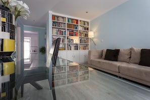 A modern living room with a glass coffee table, a beige sofa, a bookshelf, and a lamp. - Apartment with a private terrace in Bairro Alto (Lisboa)