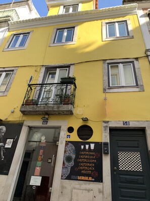 A yellow building with a black door, a balcony with plants, and a sign for Novatergulia Bar. - Apartment with a private terrace in Bairro Alto (Lisboa)