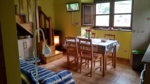 Un coin repas avec une table dressée pour quatre personnes, des chaises en bois, un téléviseur fixé au mur, une fenêtre donnant sur un paysage verdoyant et un escalier avec une rampe en bois.