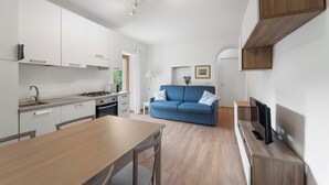 A modern kitchen with white cabinets, a dining table, and a blue sofa in the living area. - FARMHOUSE ANTICO BORGO GARDEN (COLICO)