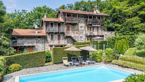 A stone building with a swimming pool, surrounded by lush greenery and a clear sky. - FARMHOUSE ANTICO BORGO GARDEN (COLICO)