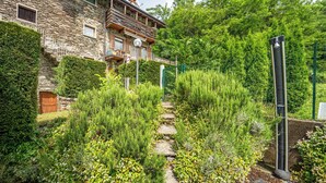 A stone building with a balcony, surrounded by lush greenery and a stone pathway. - FARMHOUSE ANTICO BORGO GARDEN (COLICO)