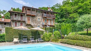 A stone building with a pool, outdoor seating, and lush greenery. - FARMHOUSE ANTICO BORGO GARDEN (COLICO)