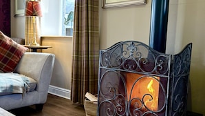 Een gezellige woonkamer met een open haard, een bank, een lamp en een raam met gordijnen.