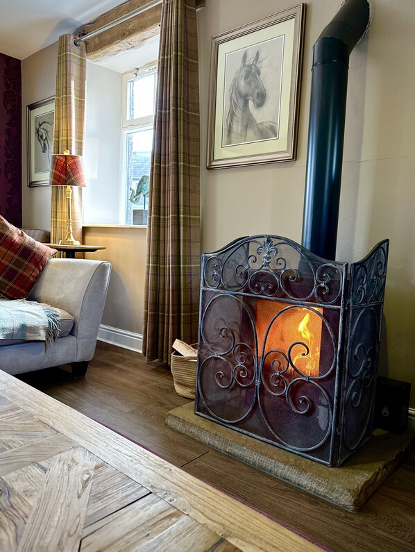 A cozy living room with a fireplace, a sofa, a lamp, and a window with curtains.