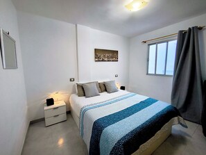 Un dormitorio con cama, mesitas de noche, un cuadro en la pared y una ventana con cortinas.
