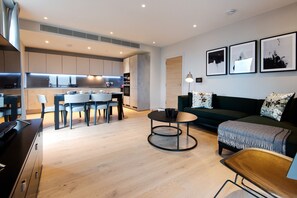 A modern living room with a sofa, coffee table, and dining area with chairs and a kitchen in the background.