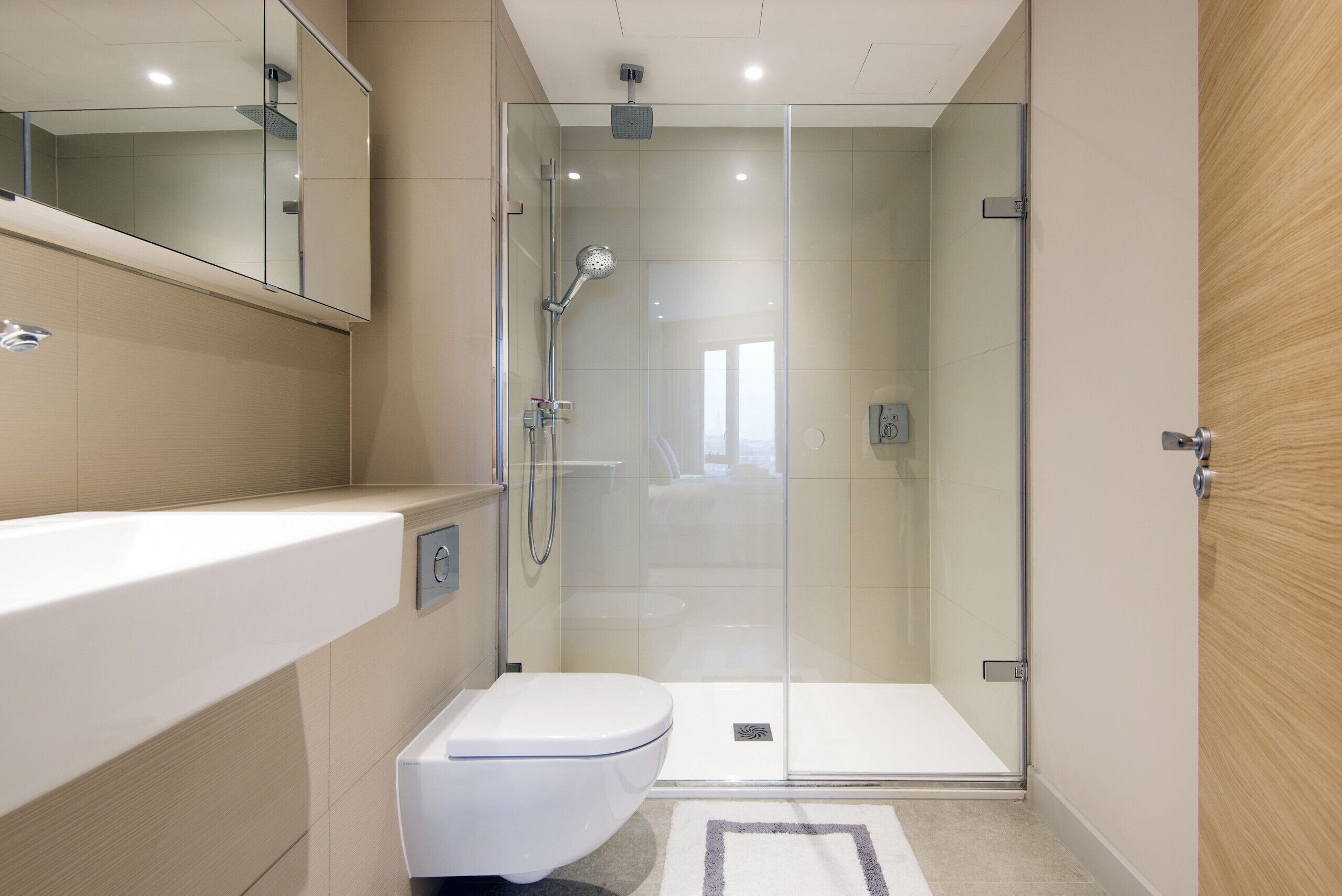 A modern bathroom with a glass-enclosed shower, a white toilet, and a large mirror above the sink.