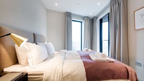 Ett hotellrum med en stor säng, en sänglampa, ett fönster med gardiner och en inramad tavla på väggen.