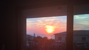 Blick auf einen Sonnenuntergang von einem Zimmer mit Holzboden und einem Fenster, das auf einen Innenhof mit einem Gebäude und einem Zaun blickt.