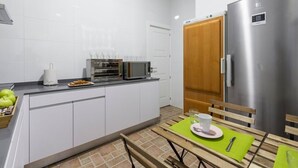 Een moderne keuken met witte kasten, een roestvrijstalen koelkast, een magnetron en een broodrooster. Er staat een eettafel met een groene placemat en een kop.